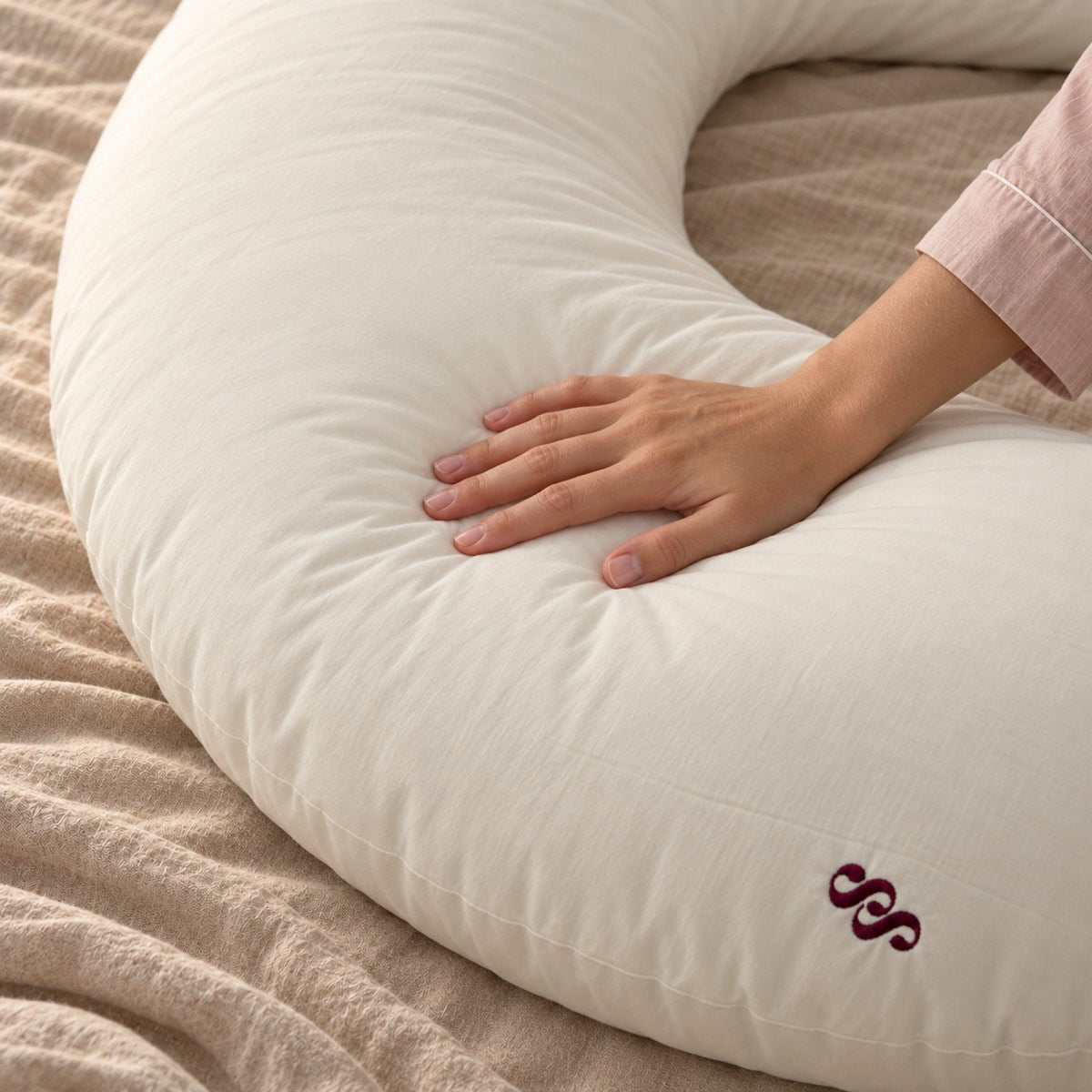Hand gently pressing the ivory Sunday Hug cover beside the burgundy SS embroidery